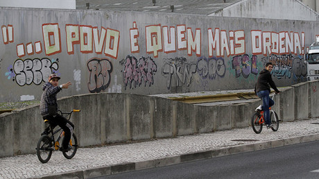 A cyclist rides past graffiti that reads 