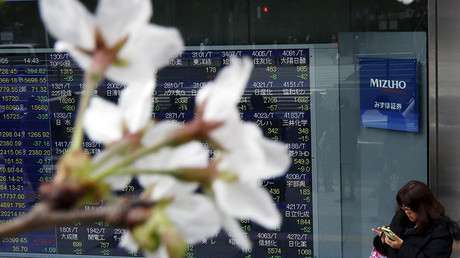 A woman uses a smart phone next to an electronic stock quotation board, as cherry blossoms bloom, outside a brokerage in Tokyo, Japan © Issei Kato