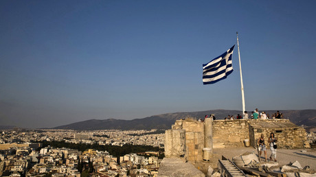 A Greek flag flutters in the wind as tourists visit the archaeological site of the Acropolis hill in Athens, Greece. © Ronen Zvulun
